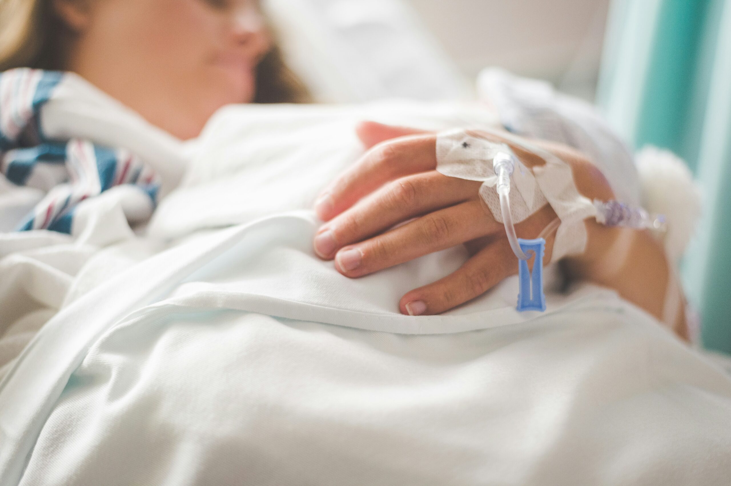 A close-up of a woman's hand with IVs in it in a hospital bed.