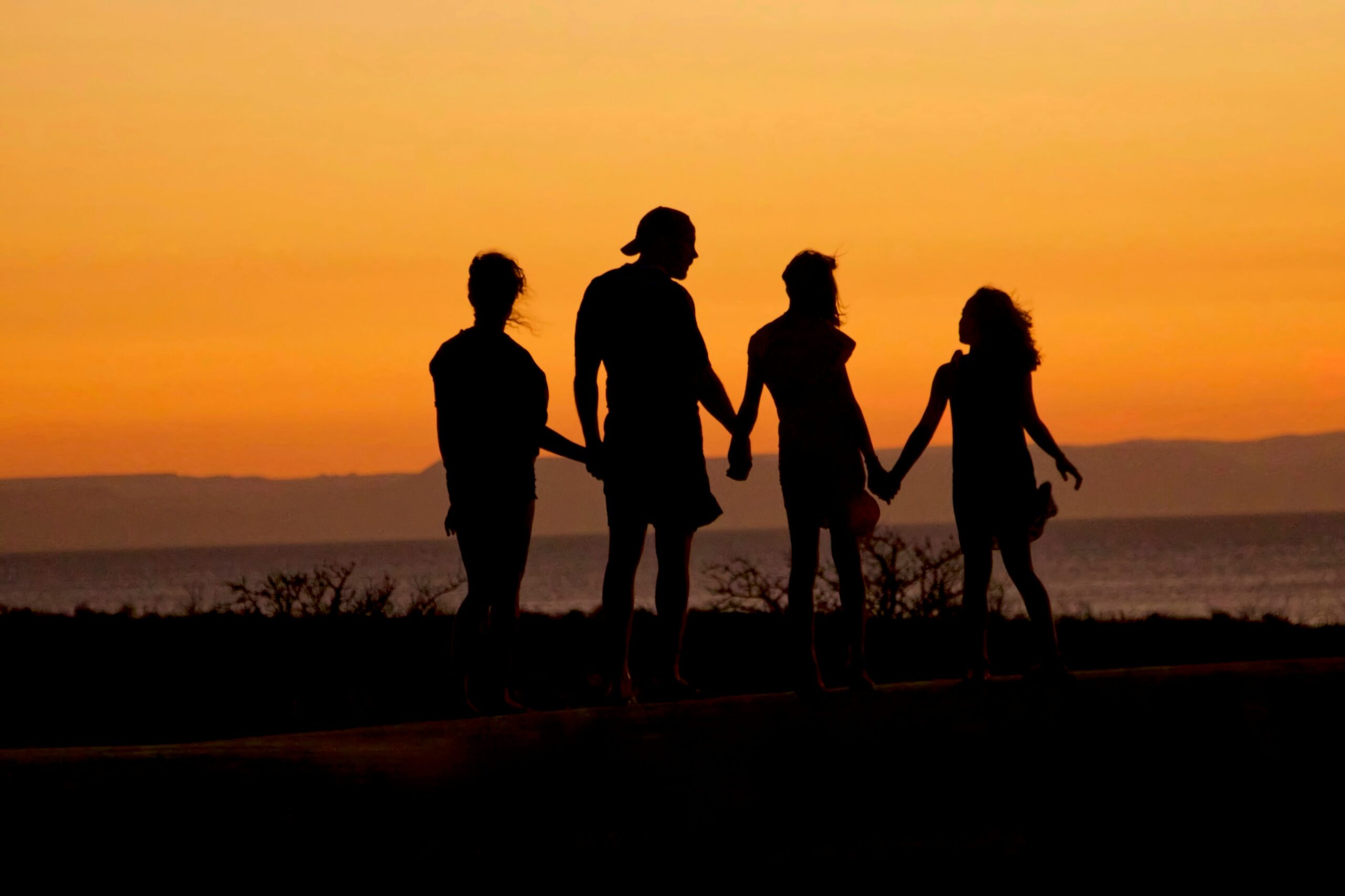 A family holds hands on the beach at sunset.