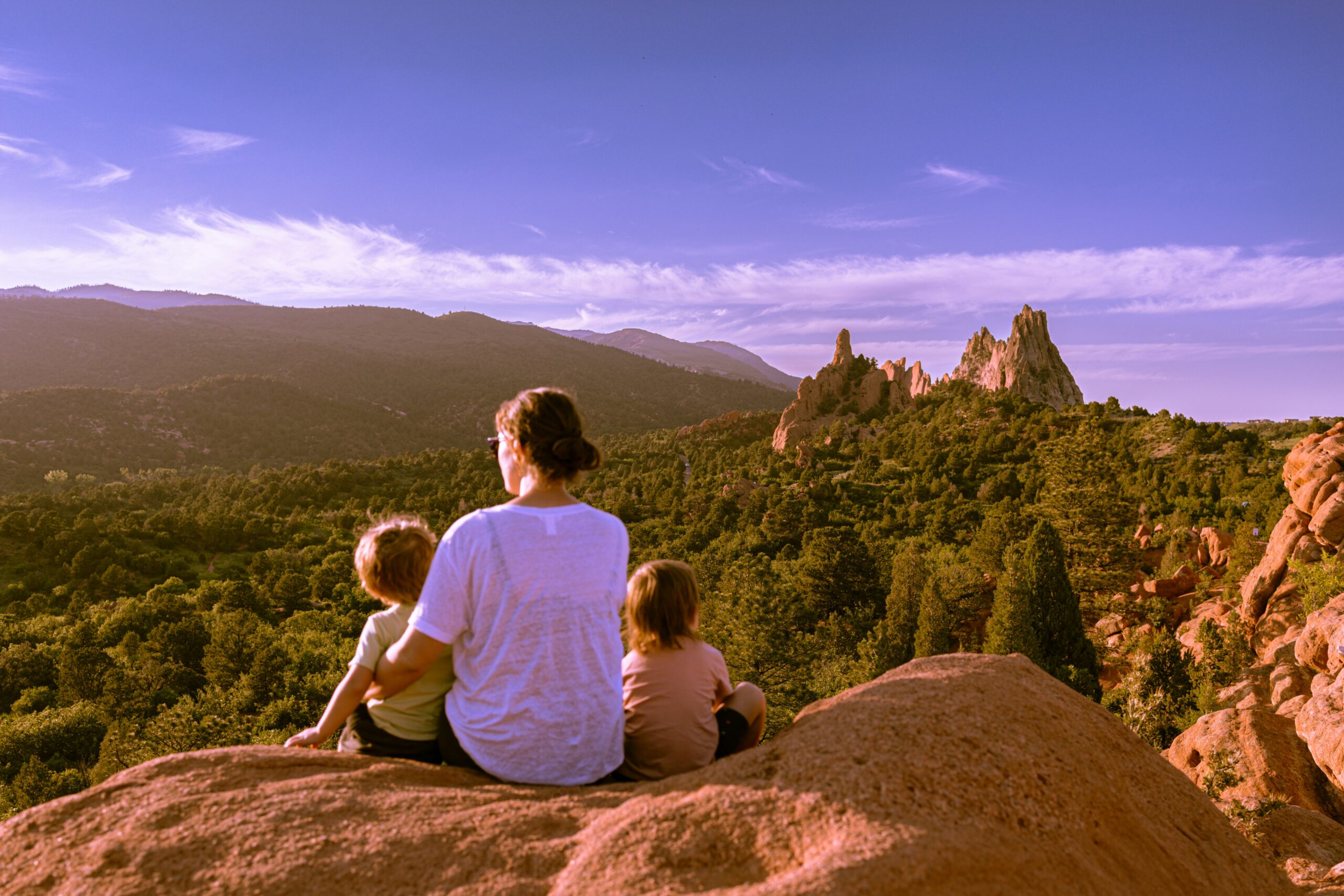 A woman and two young kids sit on a mountaintop out West.