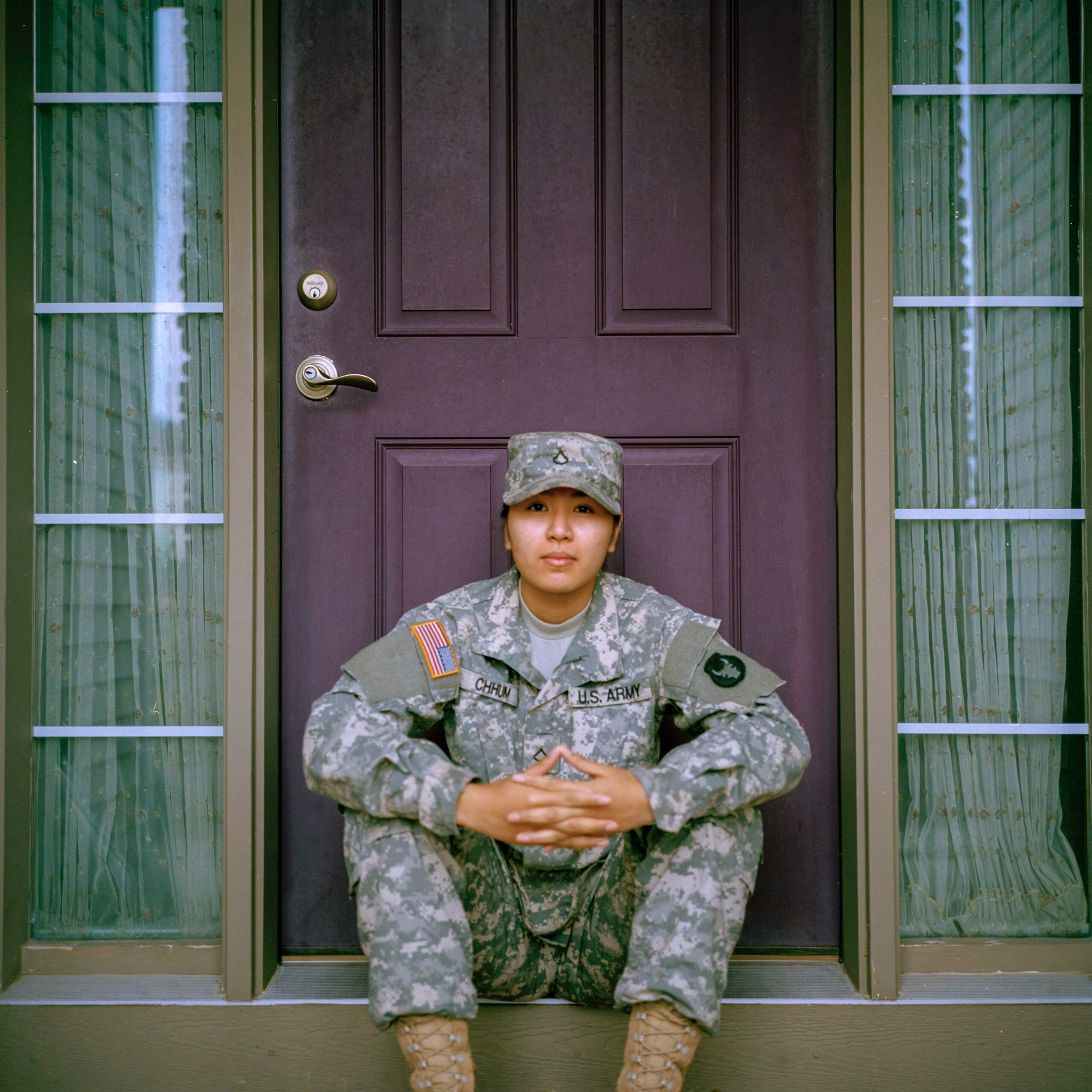 A young woman sits on a doorstep in a military uniform.