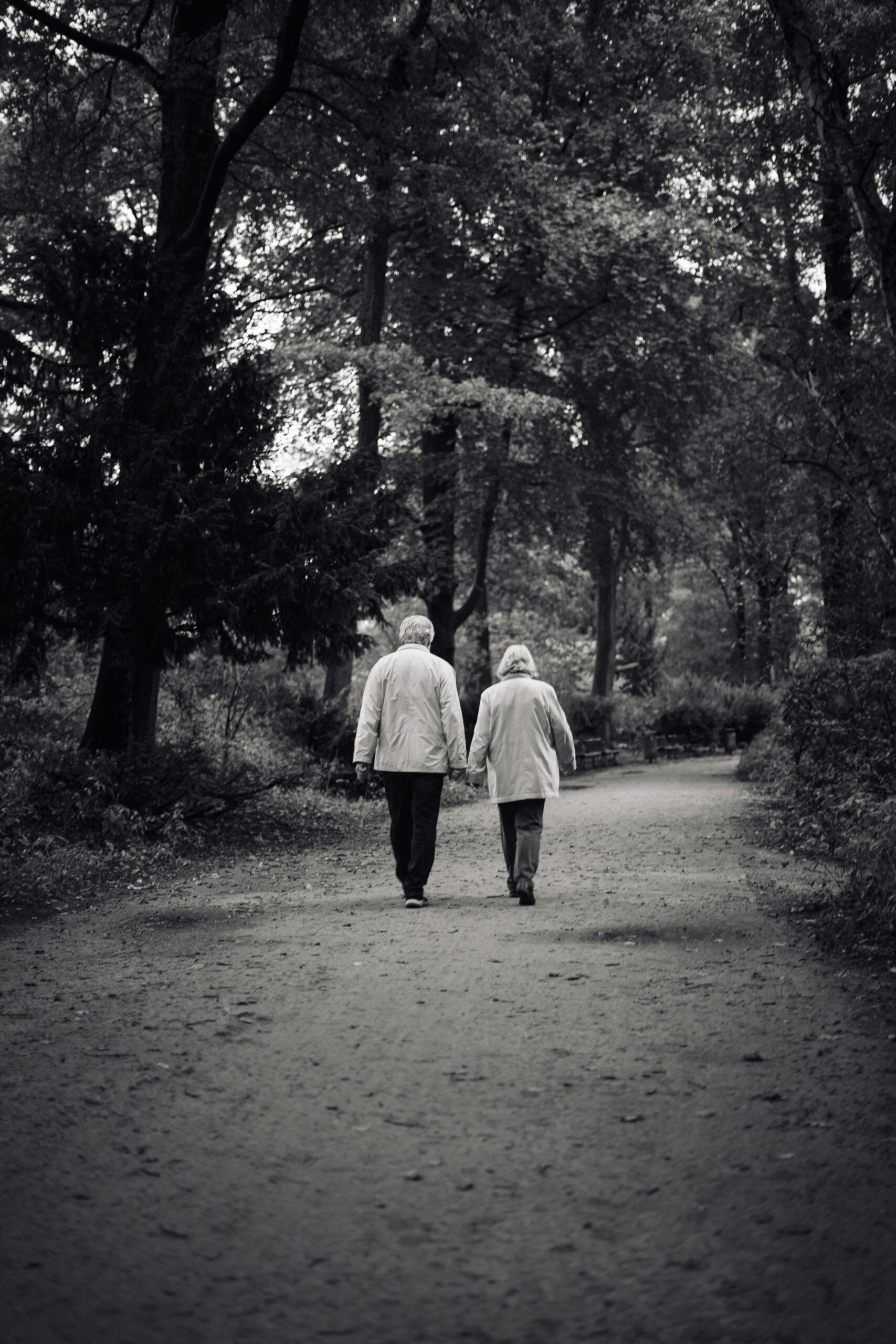 A black and white image of an old couple walking down the road.