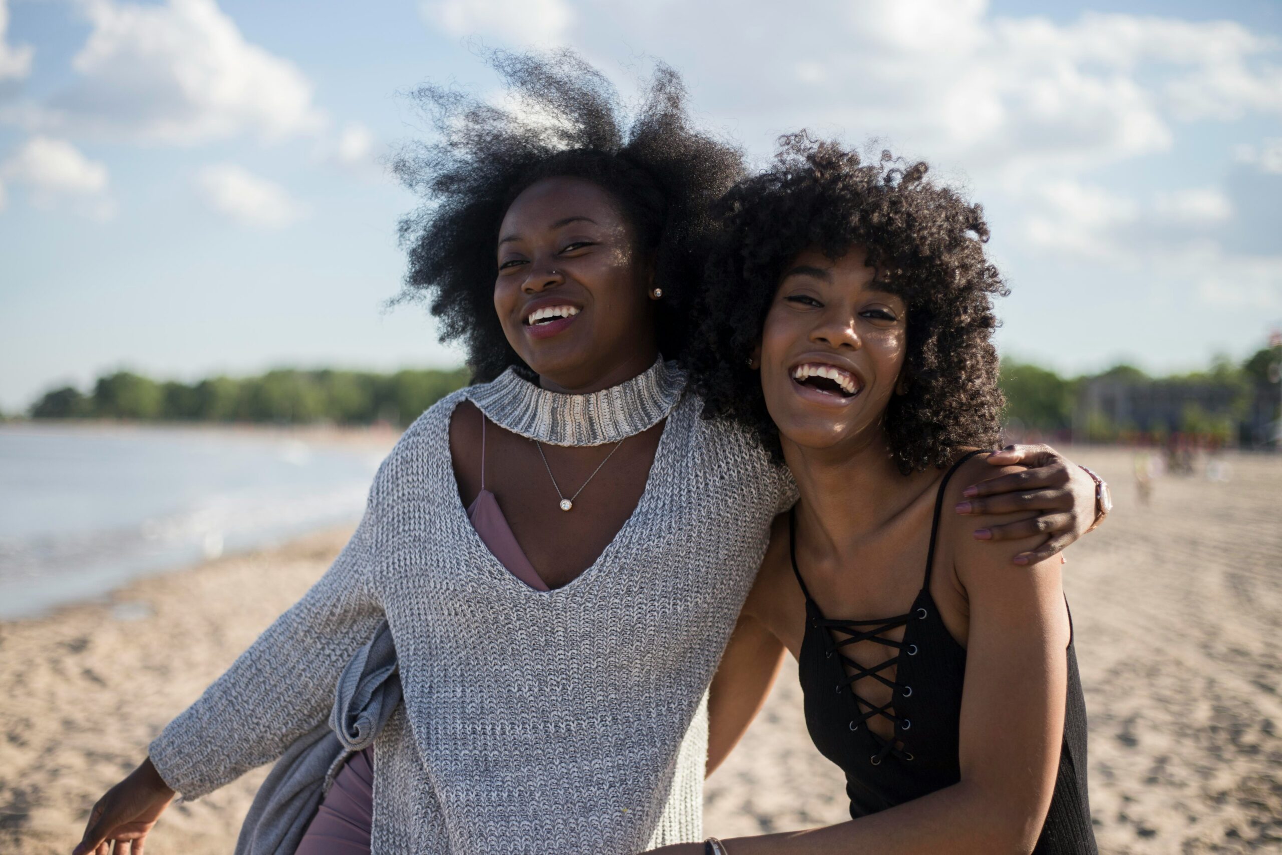 Two Black women embrace on the beach.