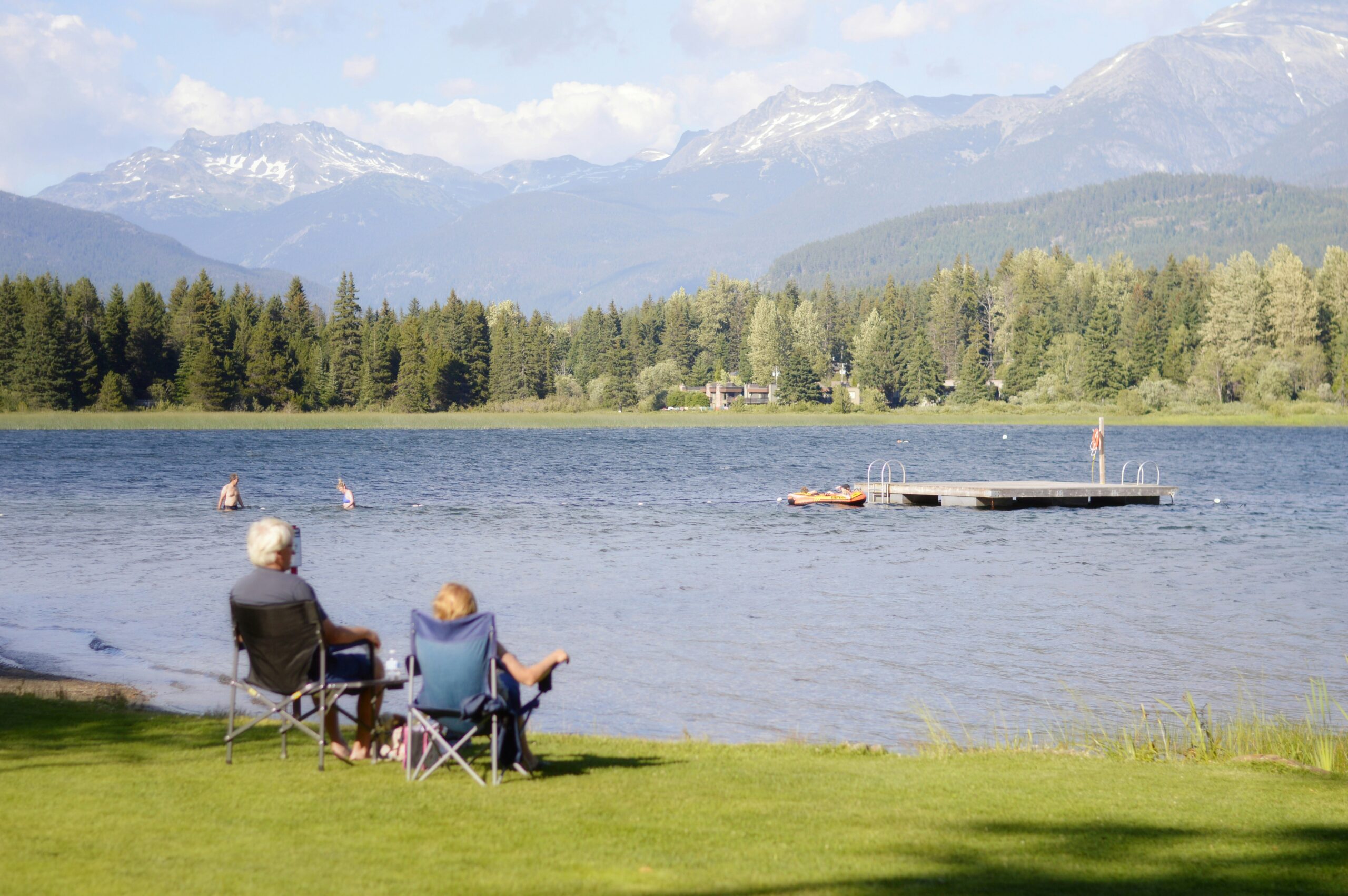 An older couple sits by a lake in the mountains.