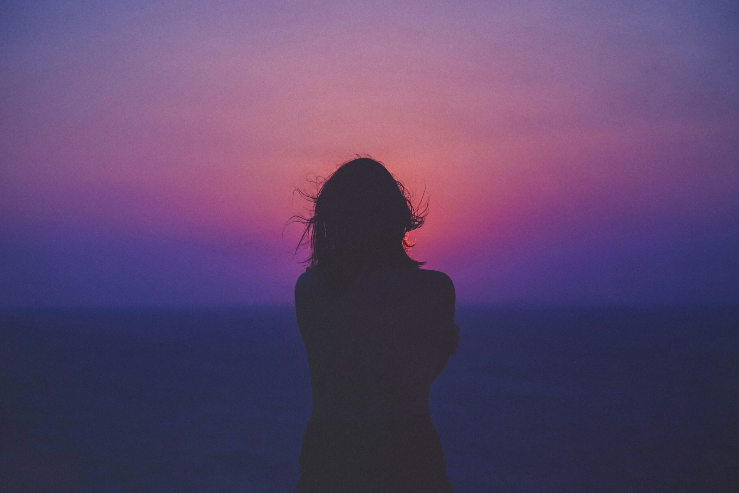 A woman from behind stands in the sunset.