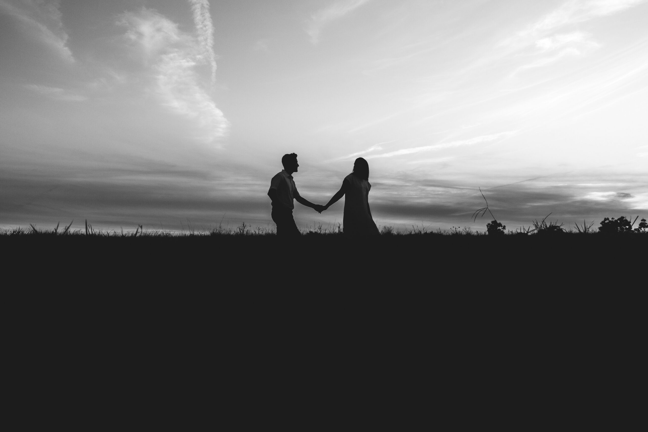 A man and woman walk hand in hand outside.